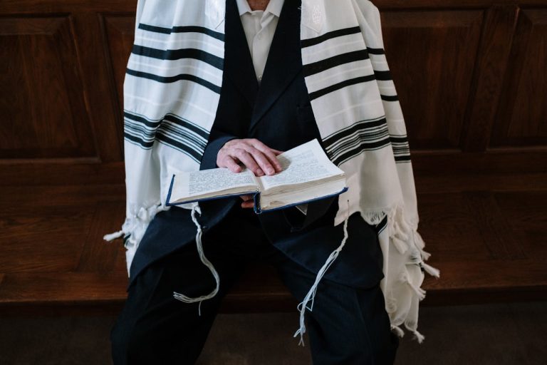Close-up of a Jewish man wearing a tallit reading a religious book in a synagogue.